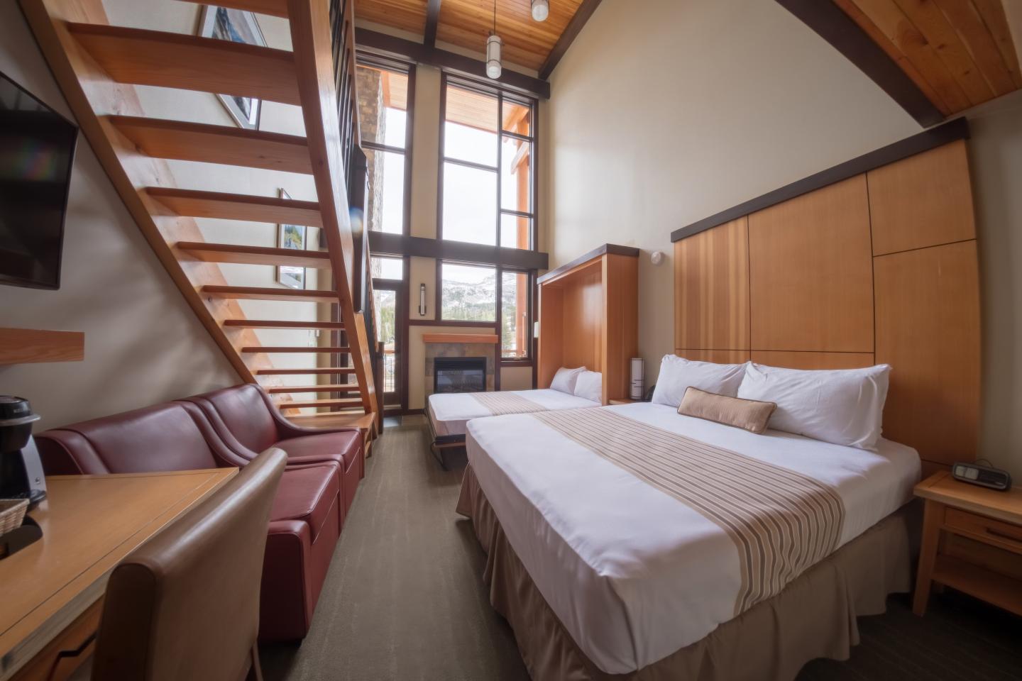 Modern loft bedroom with a double bed, wooden stairs, and high ceilings.