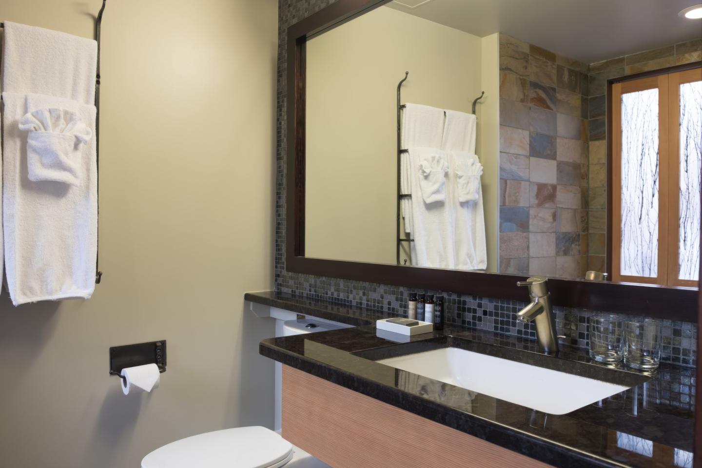Modern bathroom with double sinks, large mirror, toilet, and frosted window.