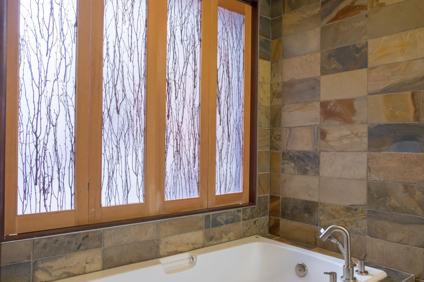 Wood-framed frosted windows above a bathtub with stone tile walls.