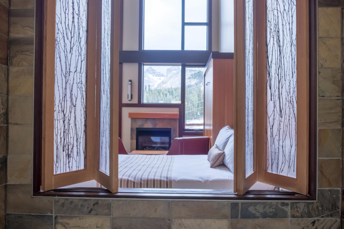 Open wooden window framing a bed and desk in a cozy room