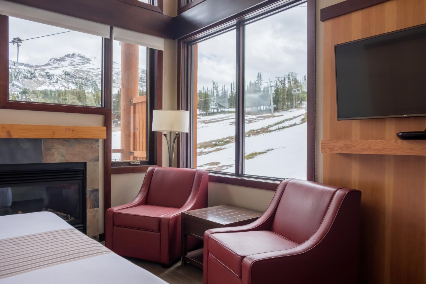 Cozy hotel room with red chairs, fireplace, mountain view.