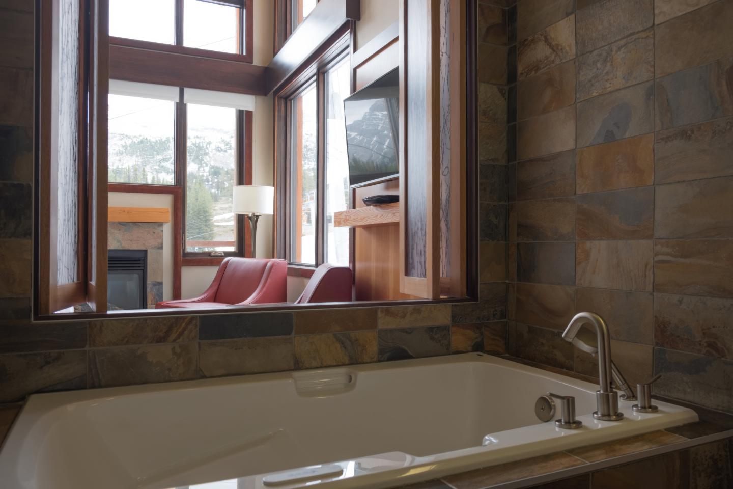Bathtub facing living area with red sofa and TV near large windows.