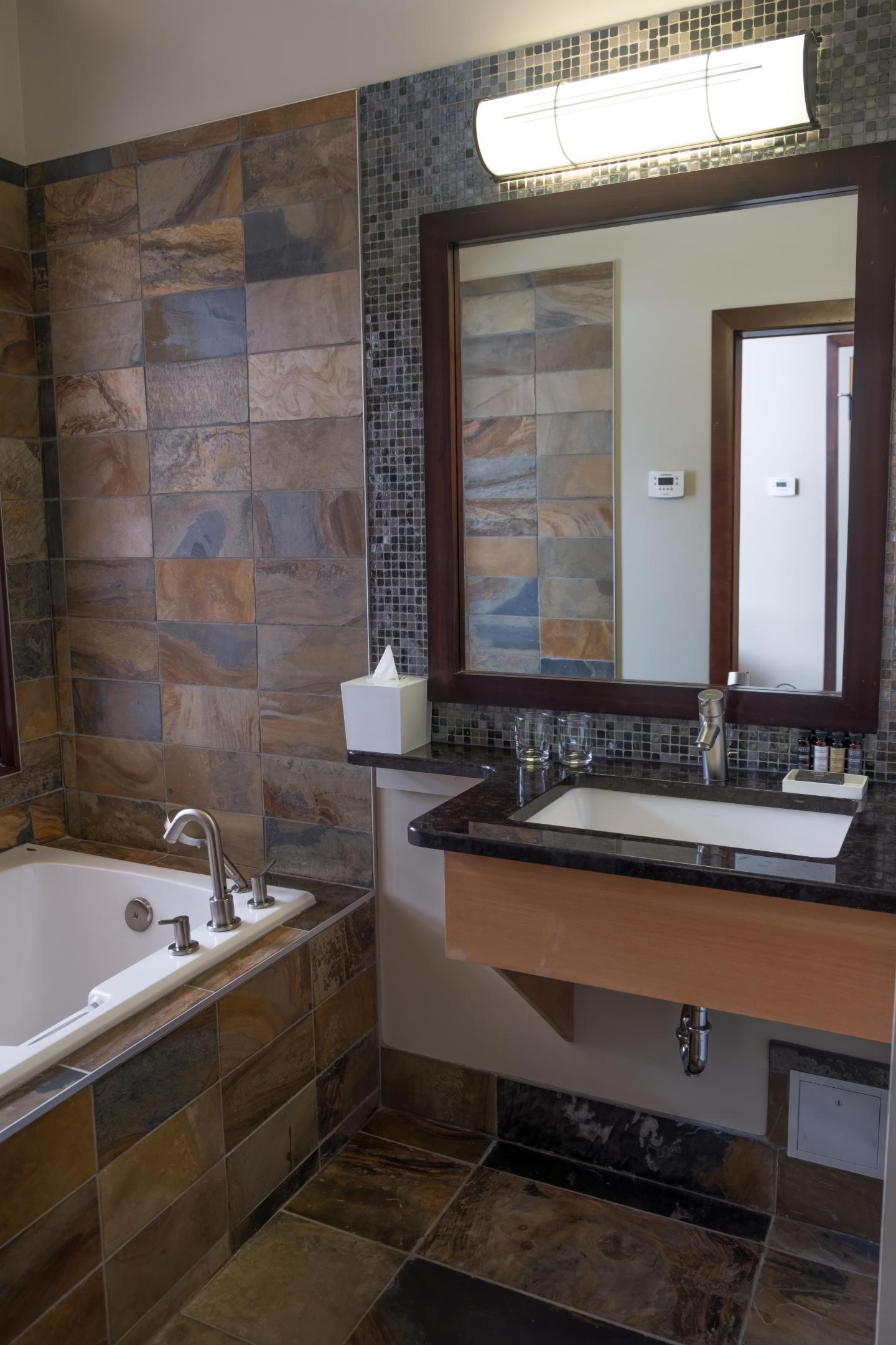 Modern bathroom with stone tiles, a bathtub, and a mirror over a sink.