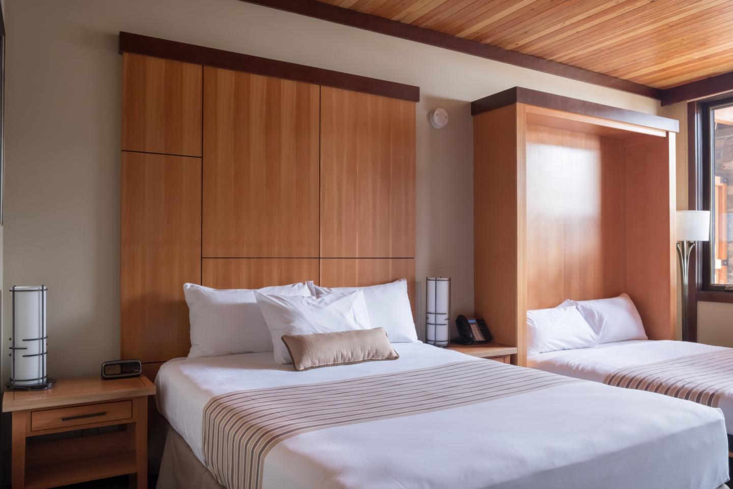 Two neatly made beds in a hotel room with wooden accents.