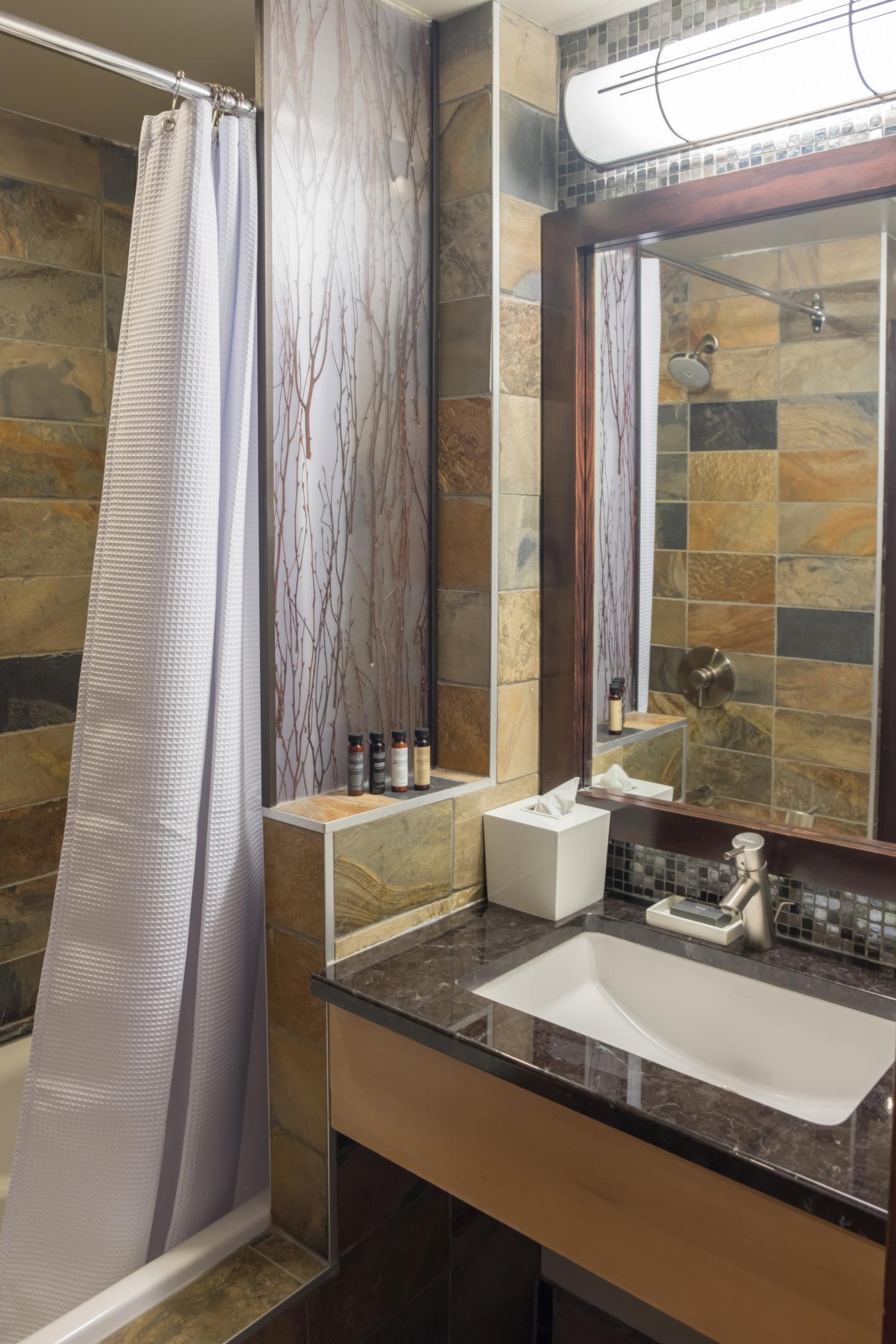 Bathroom with stone tiles, sink, mirror, and shower curtain.