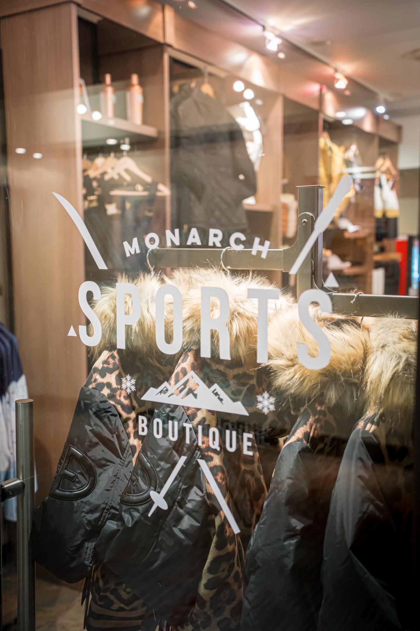 Shop window with "Monarch Sports Boutique" logo, jackets on display inside.