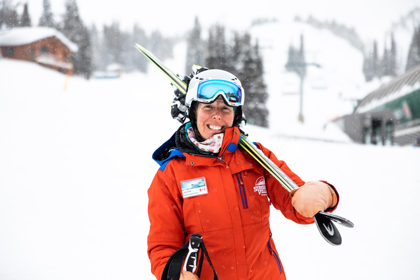 Smiling skier in red jacket holding skis on a snowy slope.