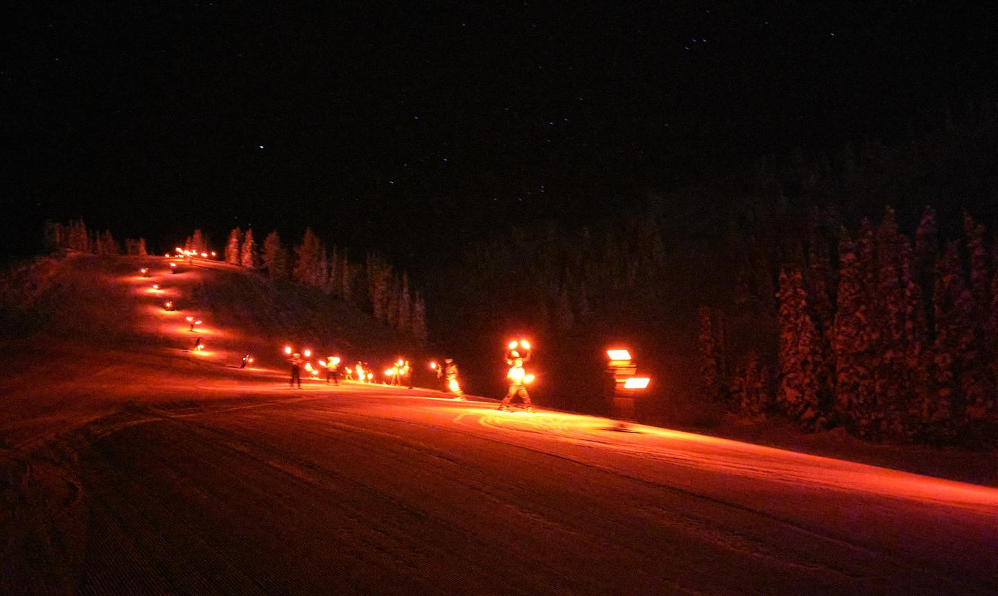 Nighttime ski run lit by a line of orange flares