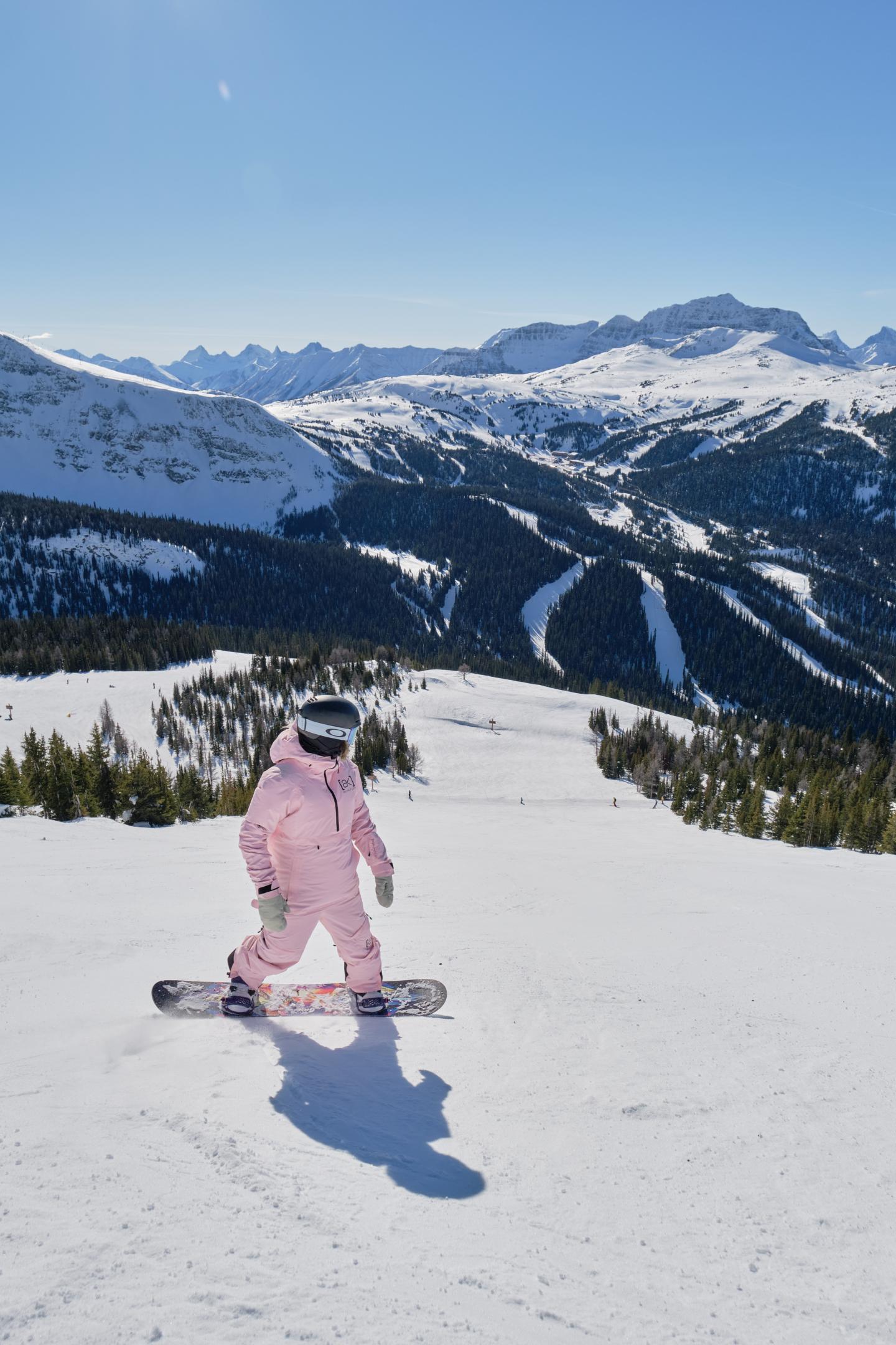 Skier in pink descends a snowy mountain slope beneath a clear blue sky.