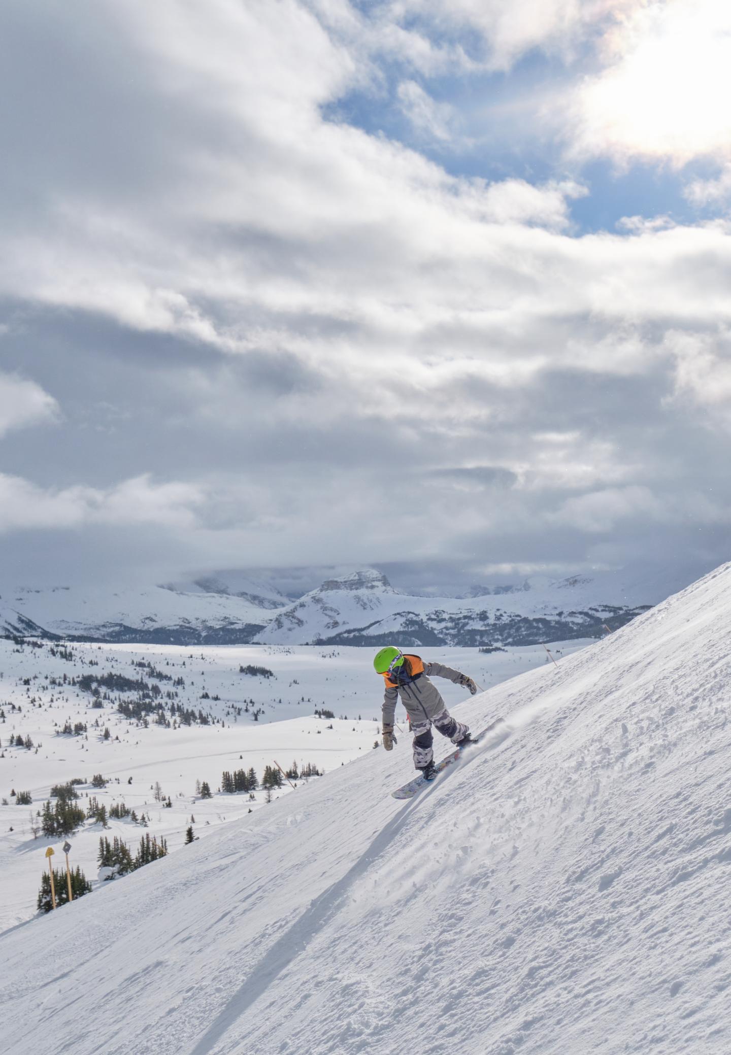 Skier in bright jacket descending a snowy mountain under cloudy skies