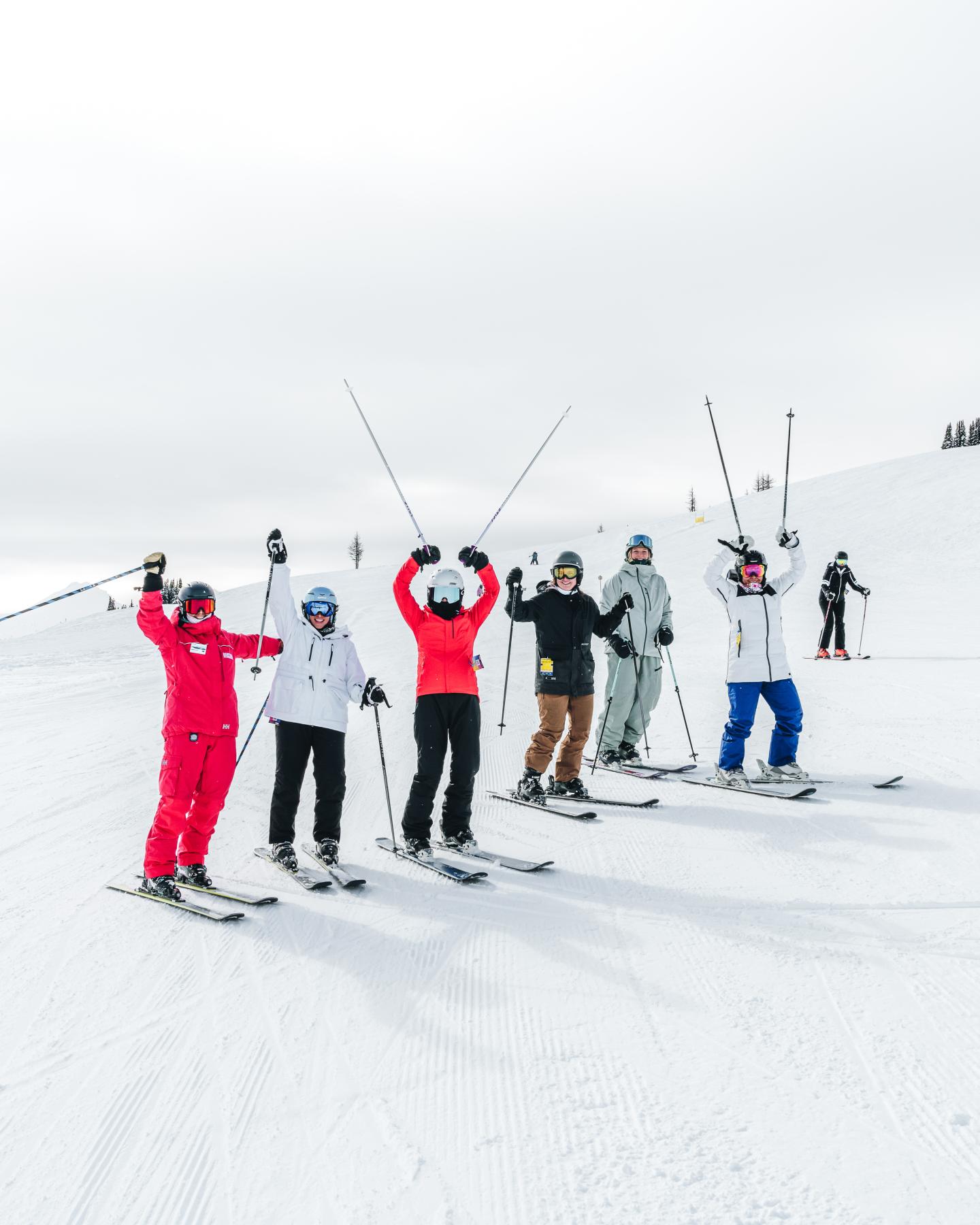 Group of skiers in colorful jackets posing with raised poles on a snowy slope