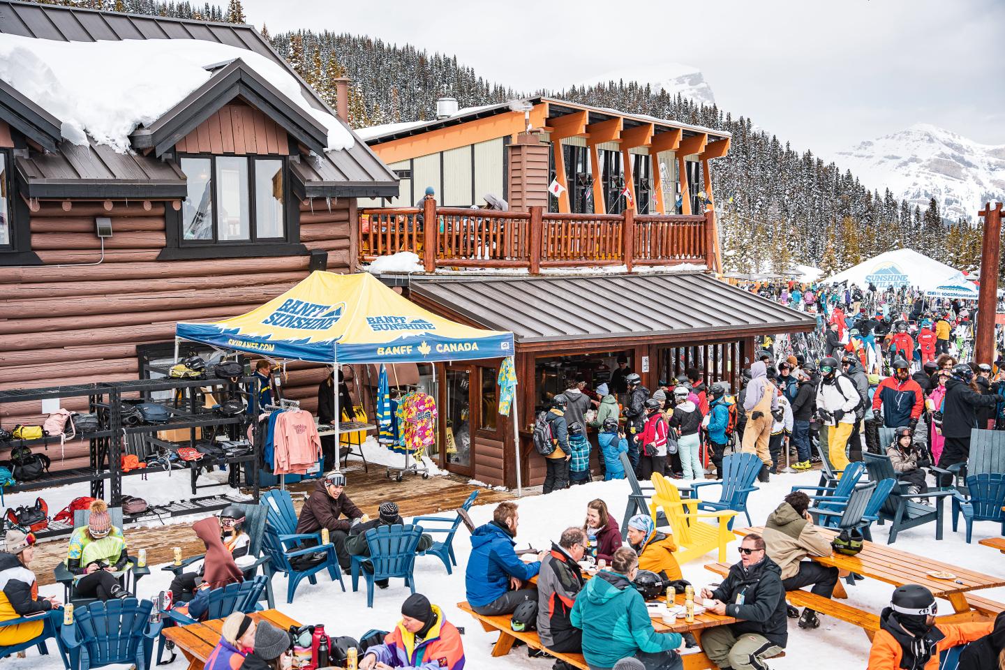 Crowded outdoor ski lodge patio with people dining and socializing in winter.