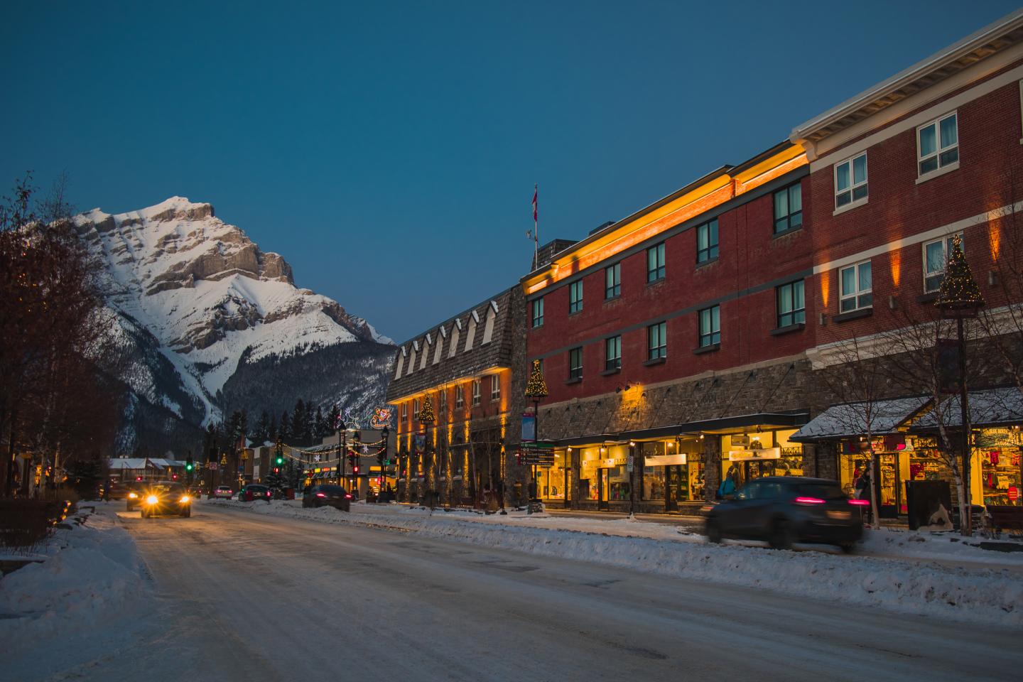 Snowy mountain street at dusk, with a red brick hotel glowing warmly.