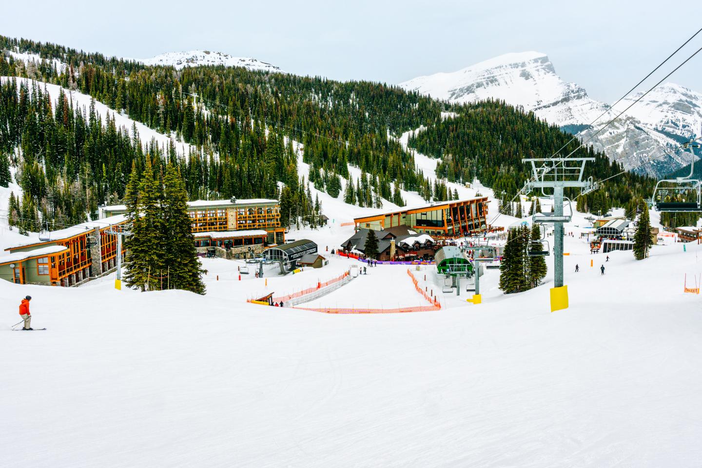 Snowy ski resort with chairlifts, skiers, and pine-covered mountains.