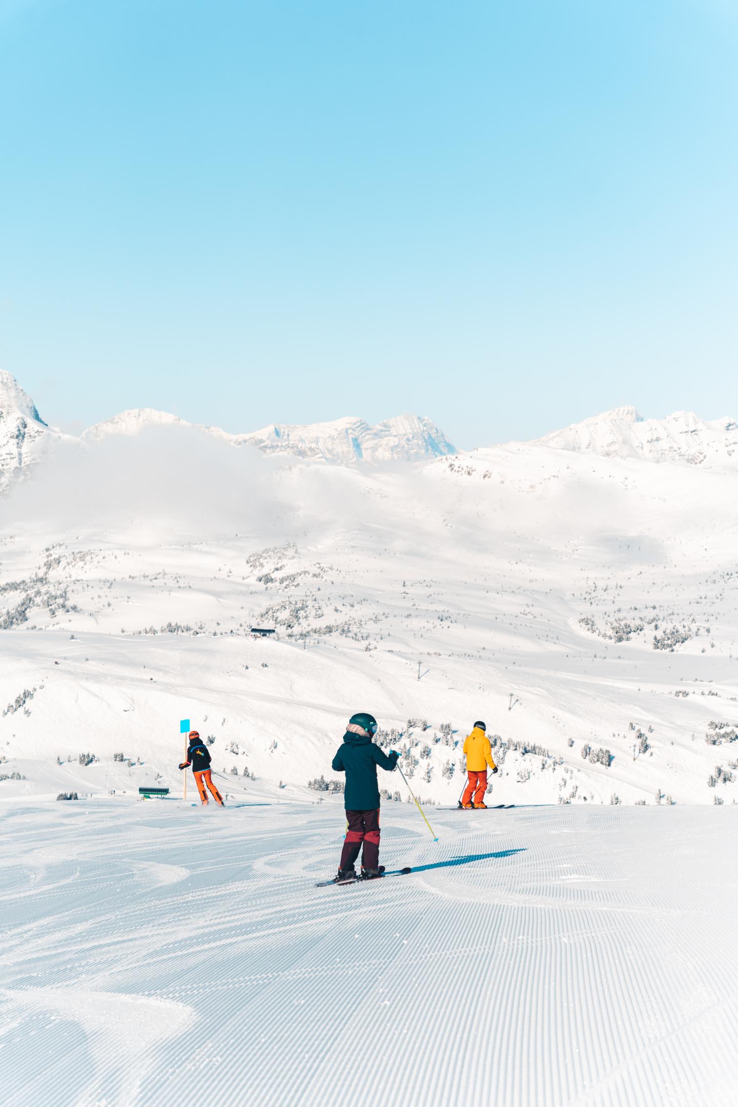 Three skiers on a snowy mountain slope beneath a clear blue sky.