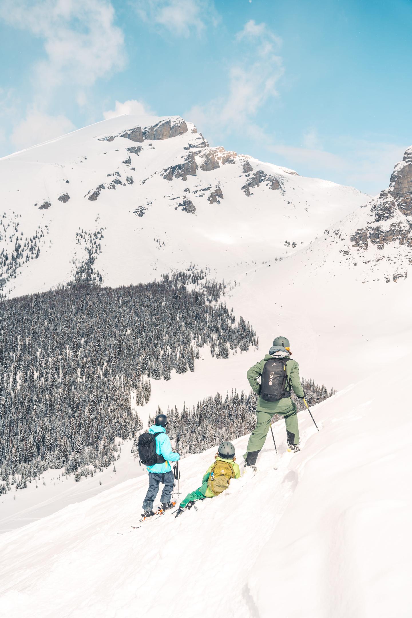 Two skiers climb a snowy mountain slope beneath a blue sky.
