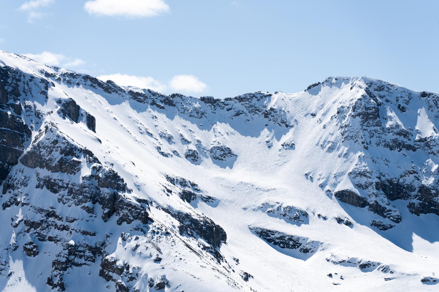 Snow-covered rocky mountain slopes beneath a clear blue sky.