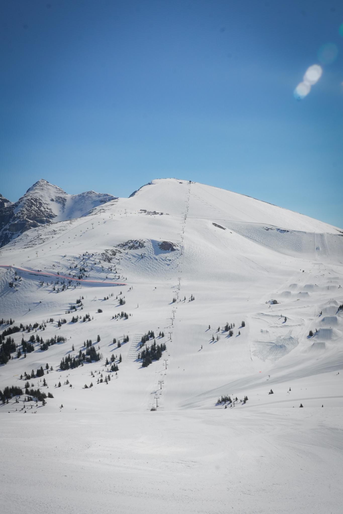 Snow-covered mountain slope under a clear blue sky, with scattered dark rocks.