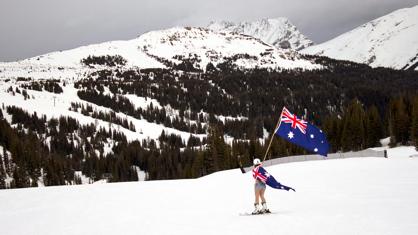 Skier holding an Australian flag on a snowy mountain slope.
