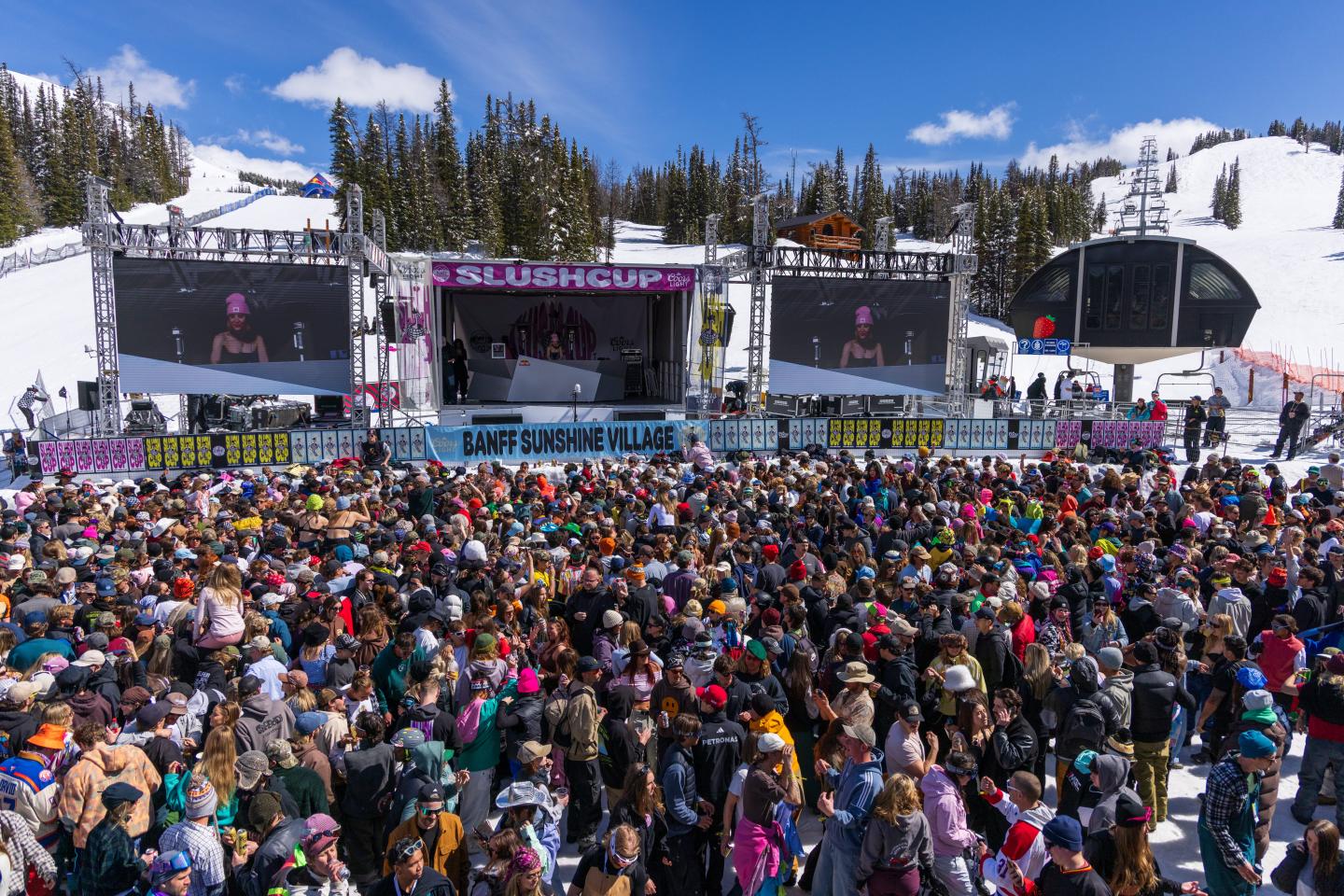 Crowd gathered before outdoor festival stages in a snowy mountain setting.