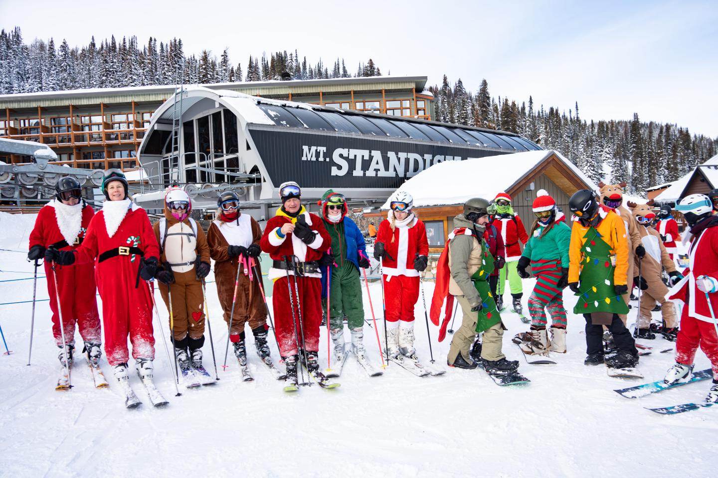 Skiers in colorful costumes gather at a snowy resort beneath an Mt. Standish sign.