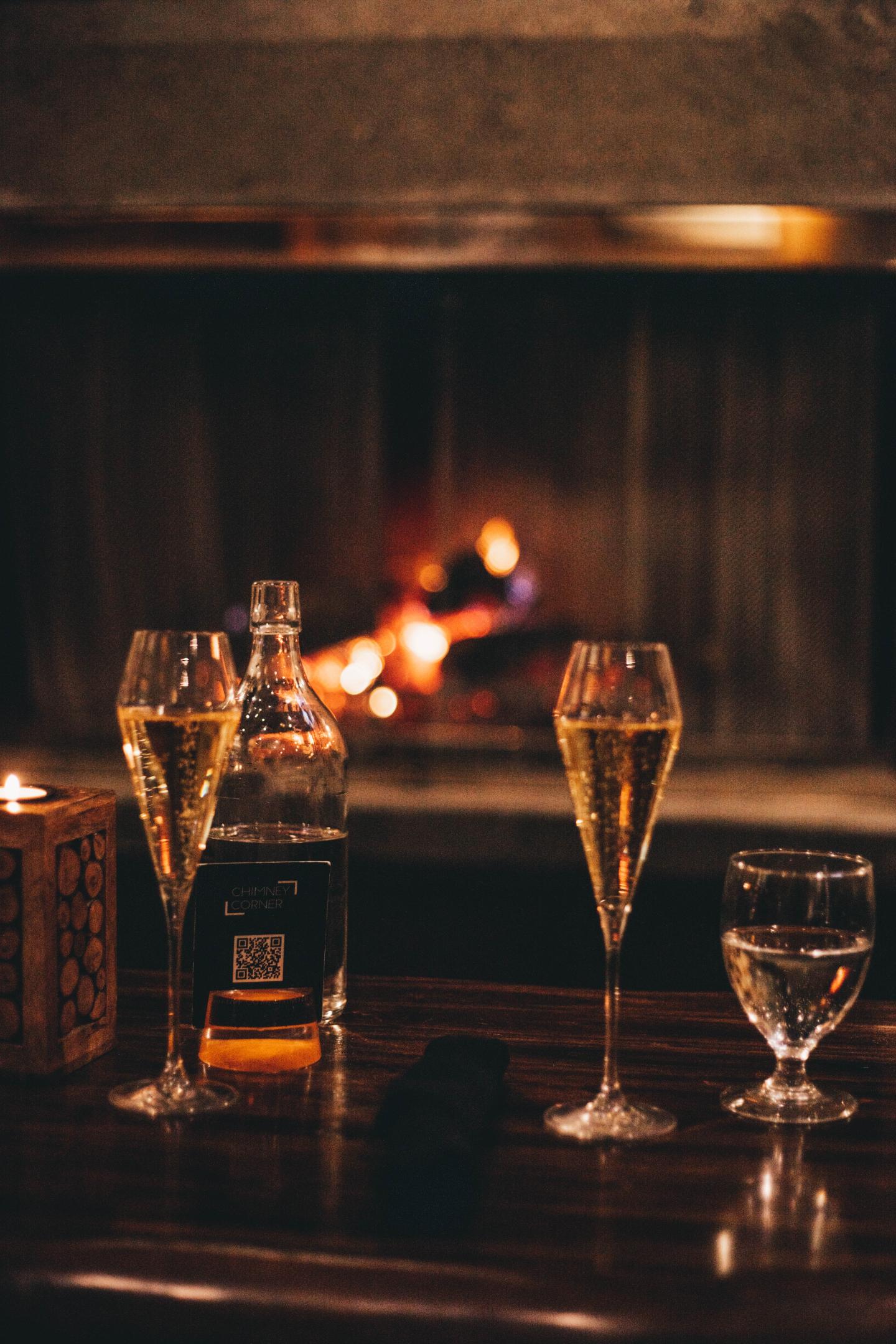 Whiskey bottle, glasses, and a cigar on a dark bar with warm candlelight.