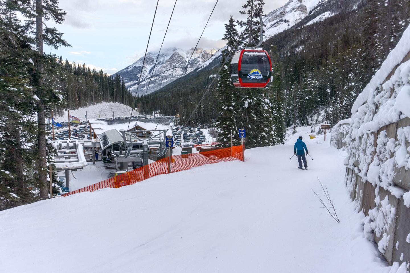 Skier on snowy mountain trail beneath a red gondola lift.