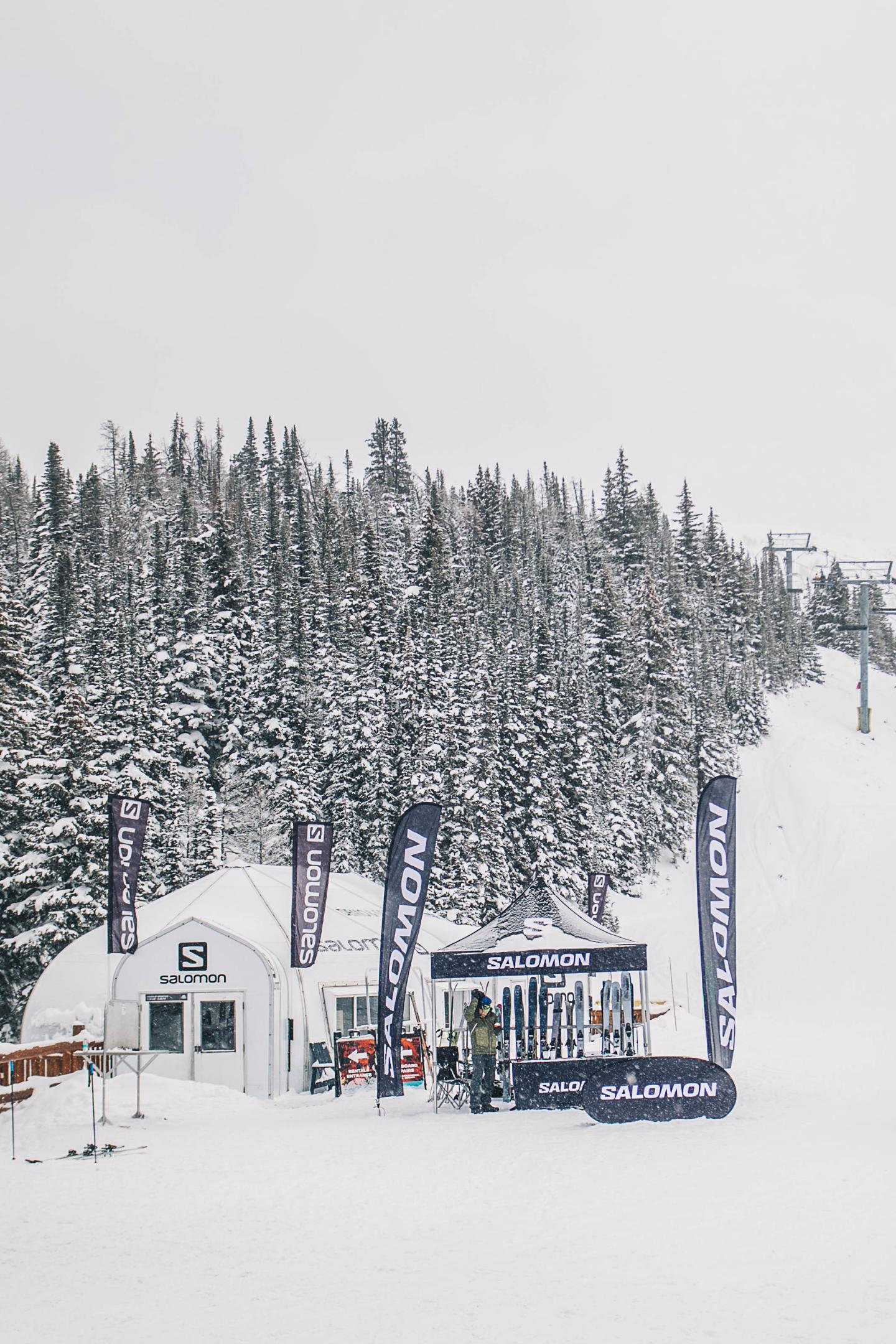 Snowy ski lift station at the base of a forested mountain.