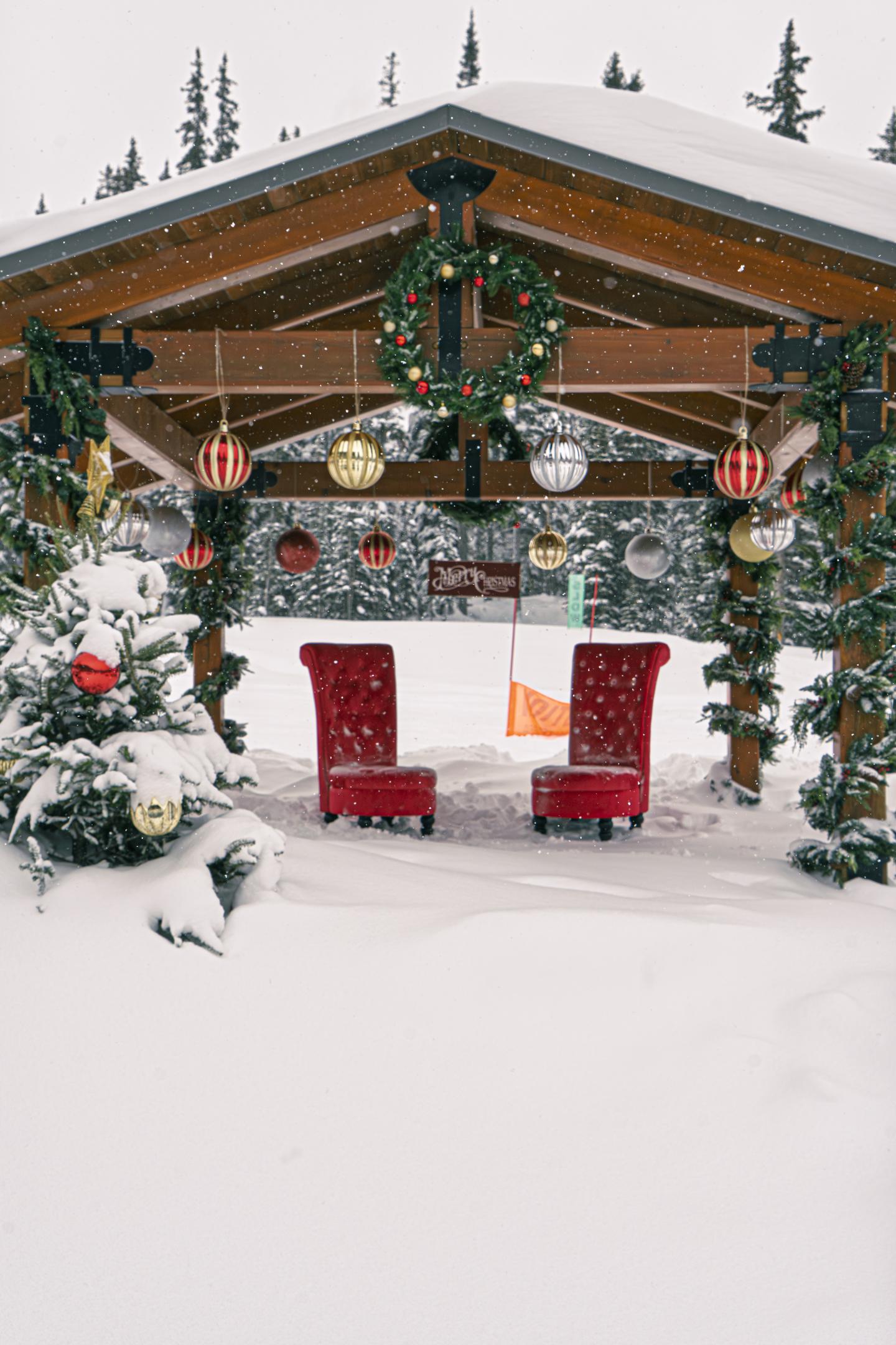 Snowy log cabin decorated with Christmas wreaths, garlands, and red chairs