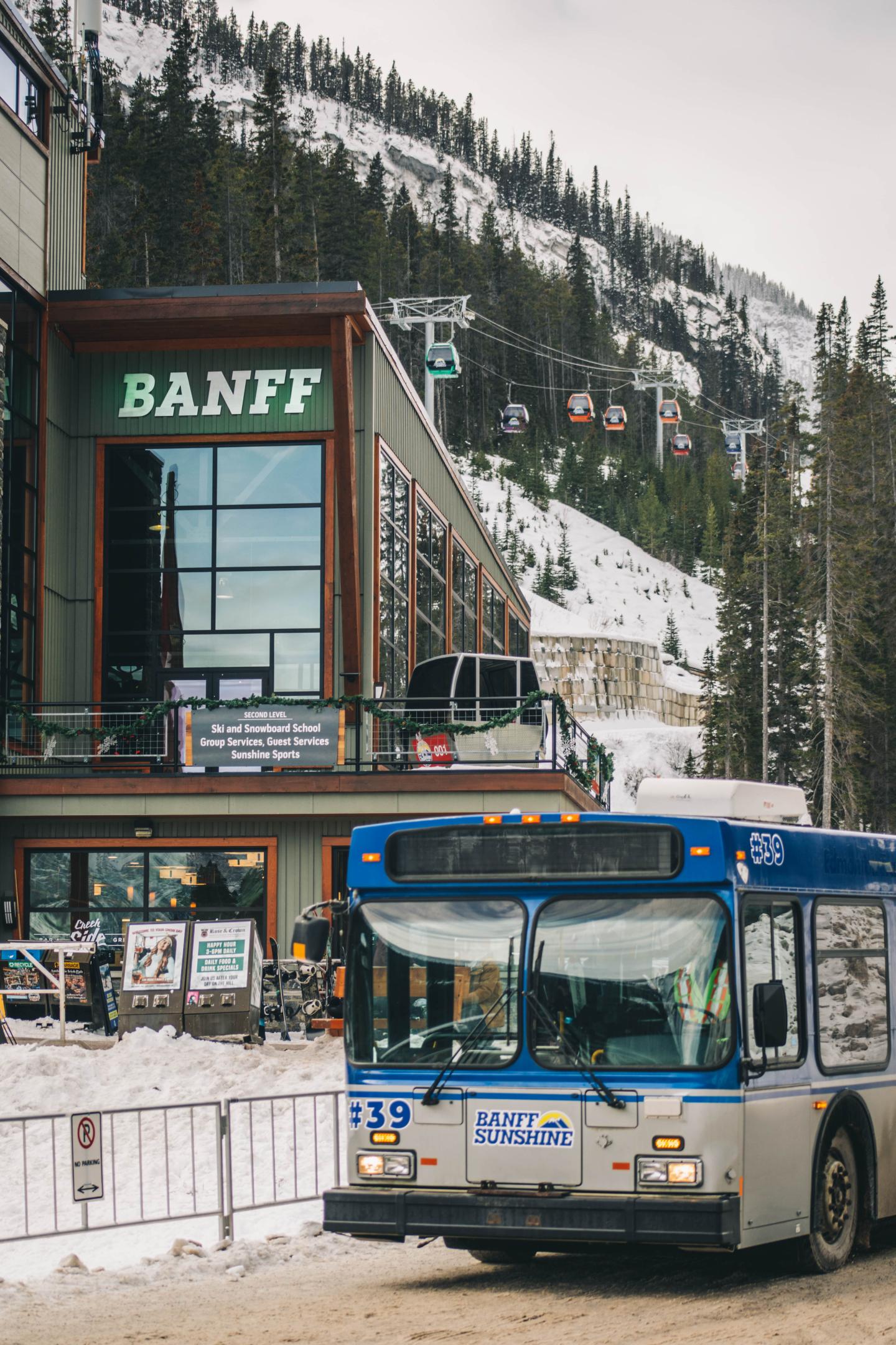 Blue and white city bus outside Banff station, with snowy mountain behind.