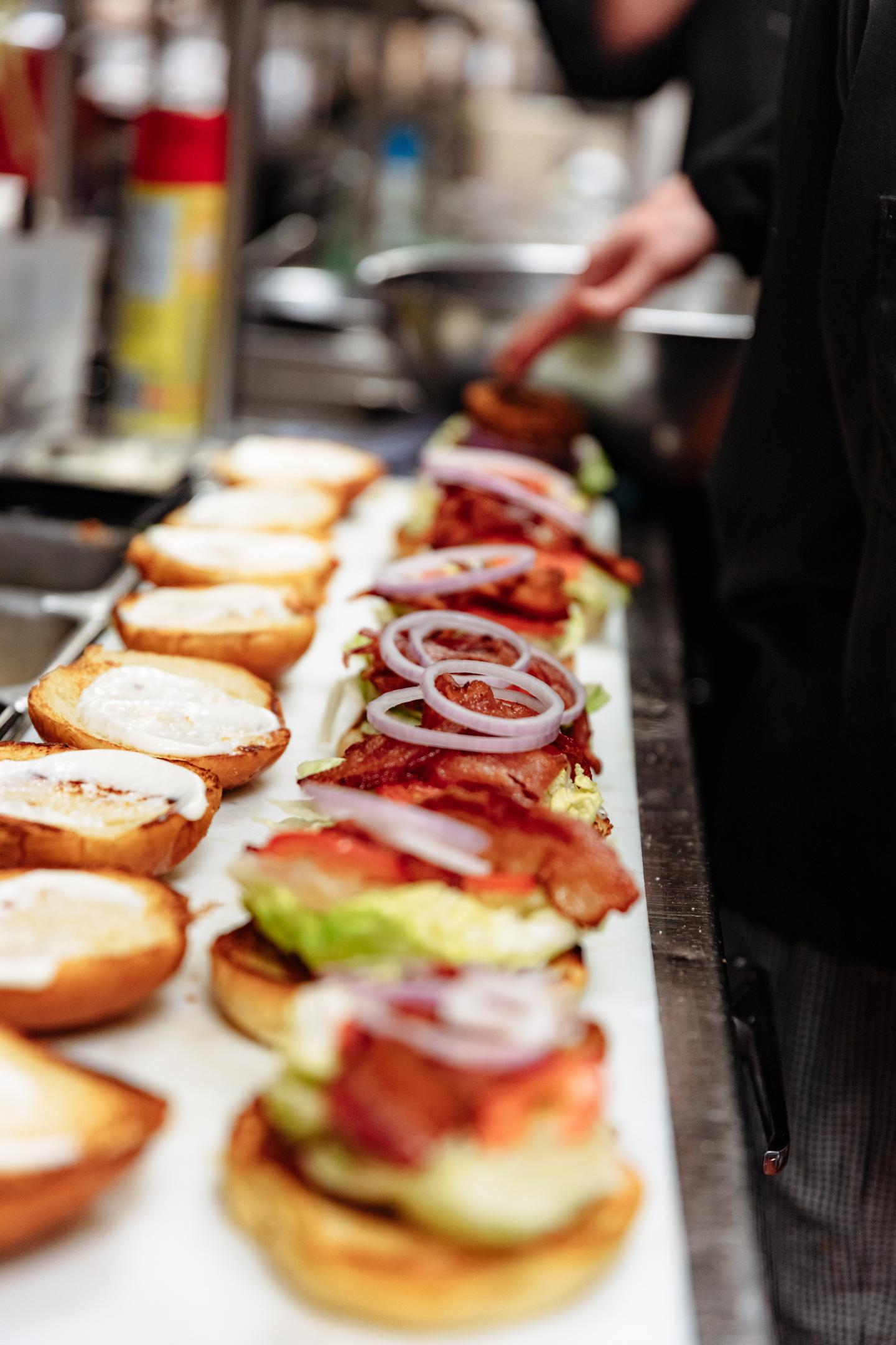 Chef preparing stacked gourmet burgers on a restaurant counter.