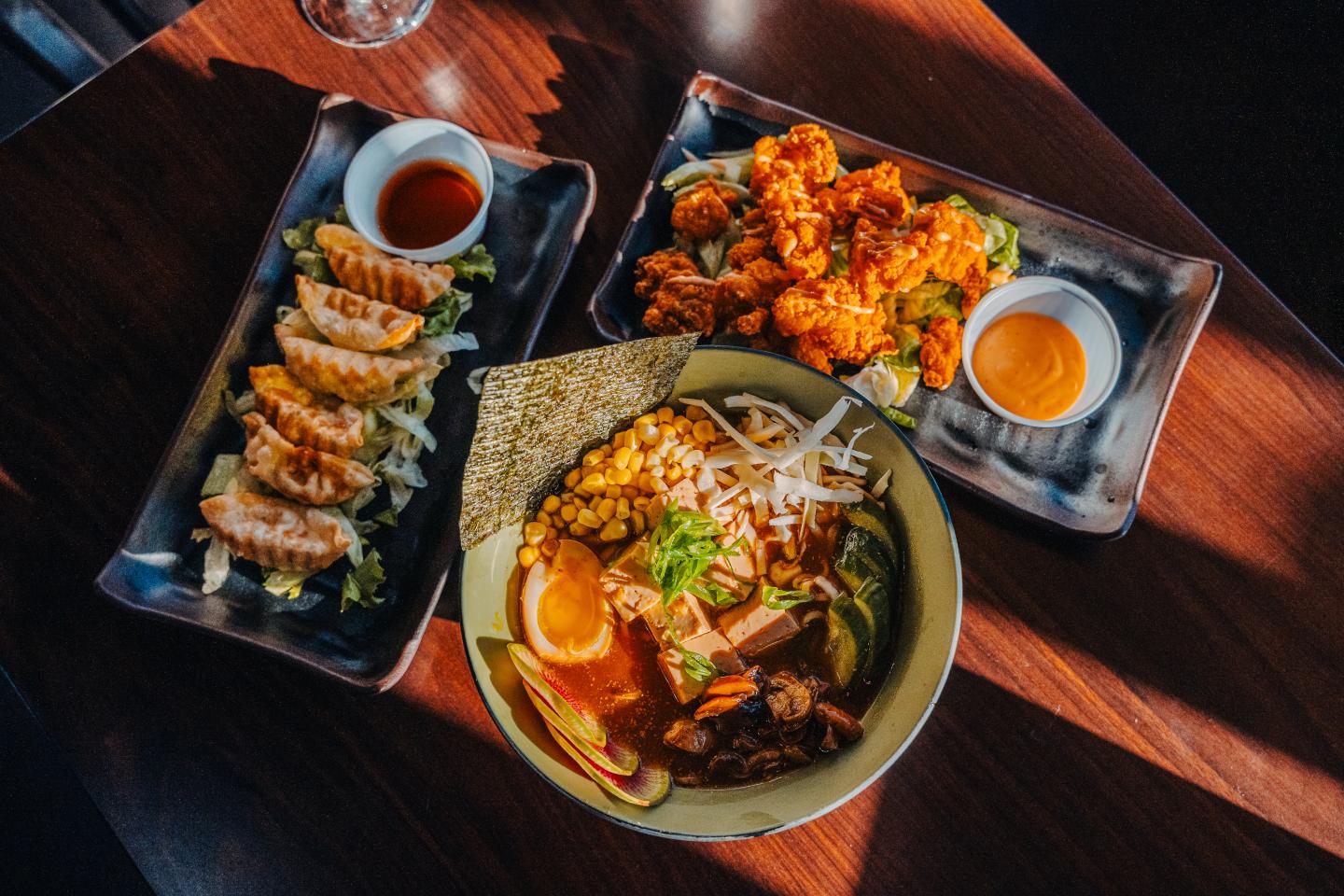 Overhead view of Asian dishes with rice, dumplings, skewers, and dipping sauces.