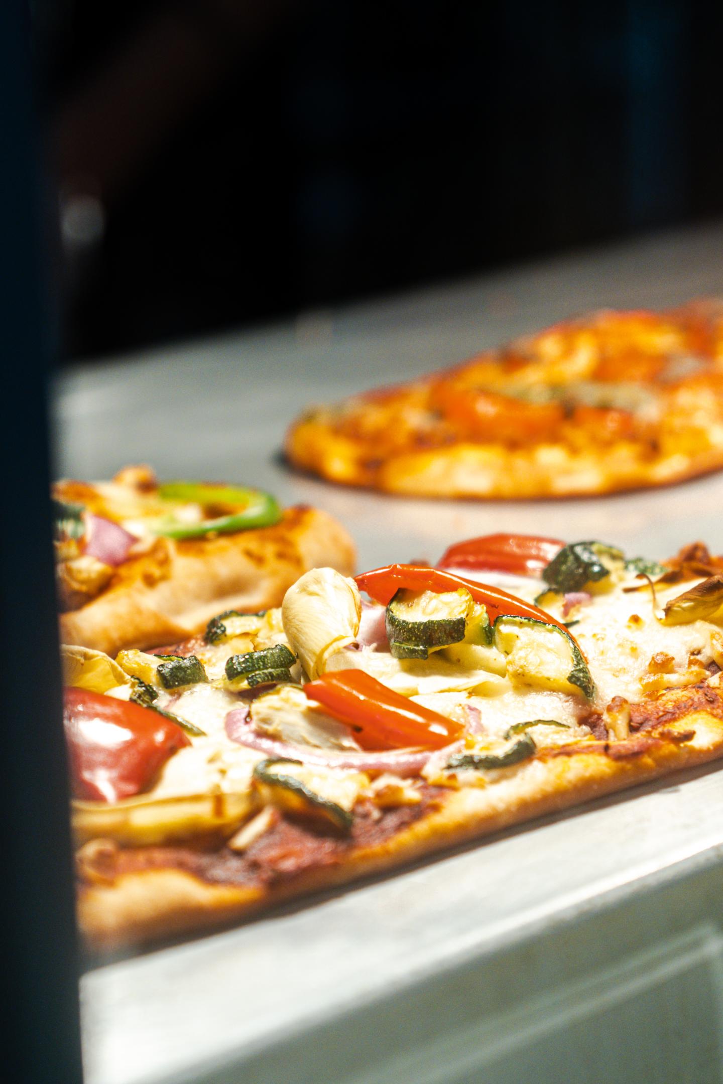 Two pizzas baking on trays inside an oven.