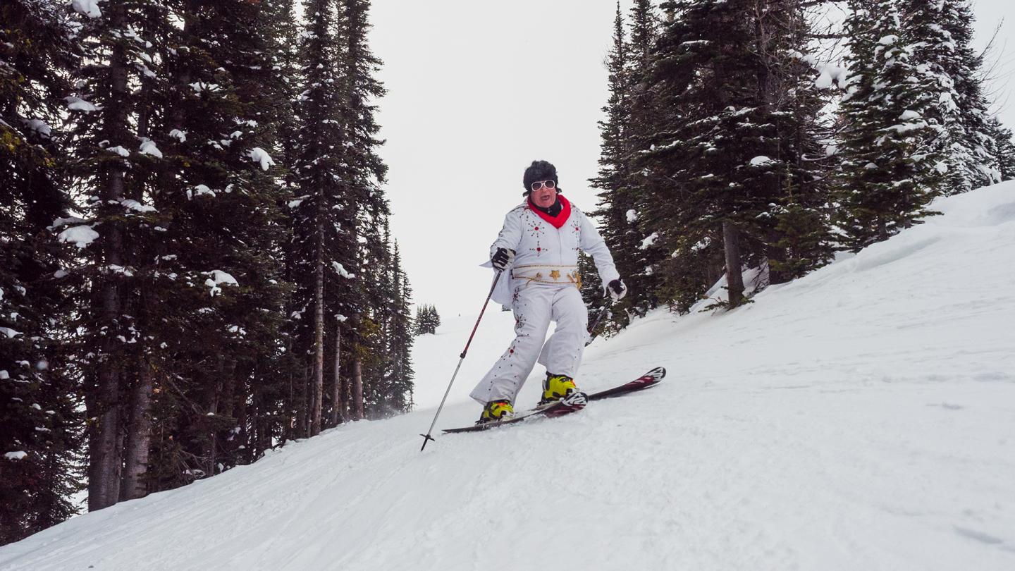 Elvis descending a snowy slope among tall pine trees.