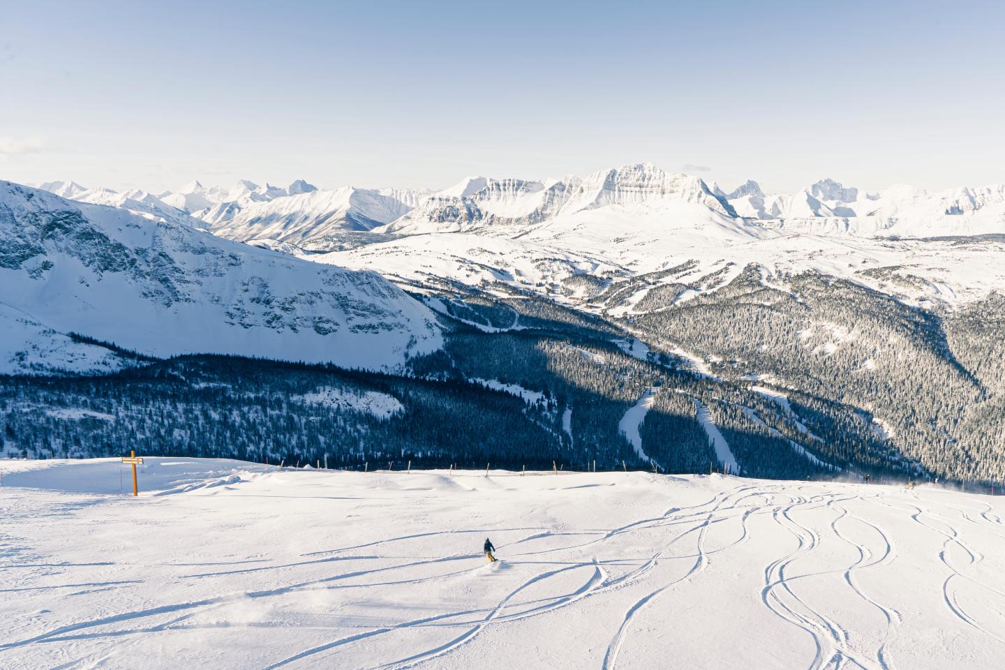 Snow-covered mountain valley with ski tracks under a clear blue sky