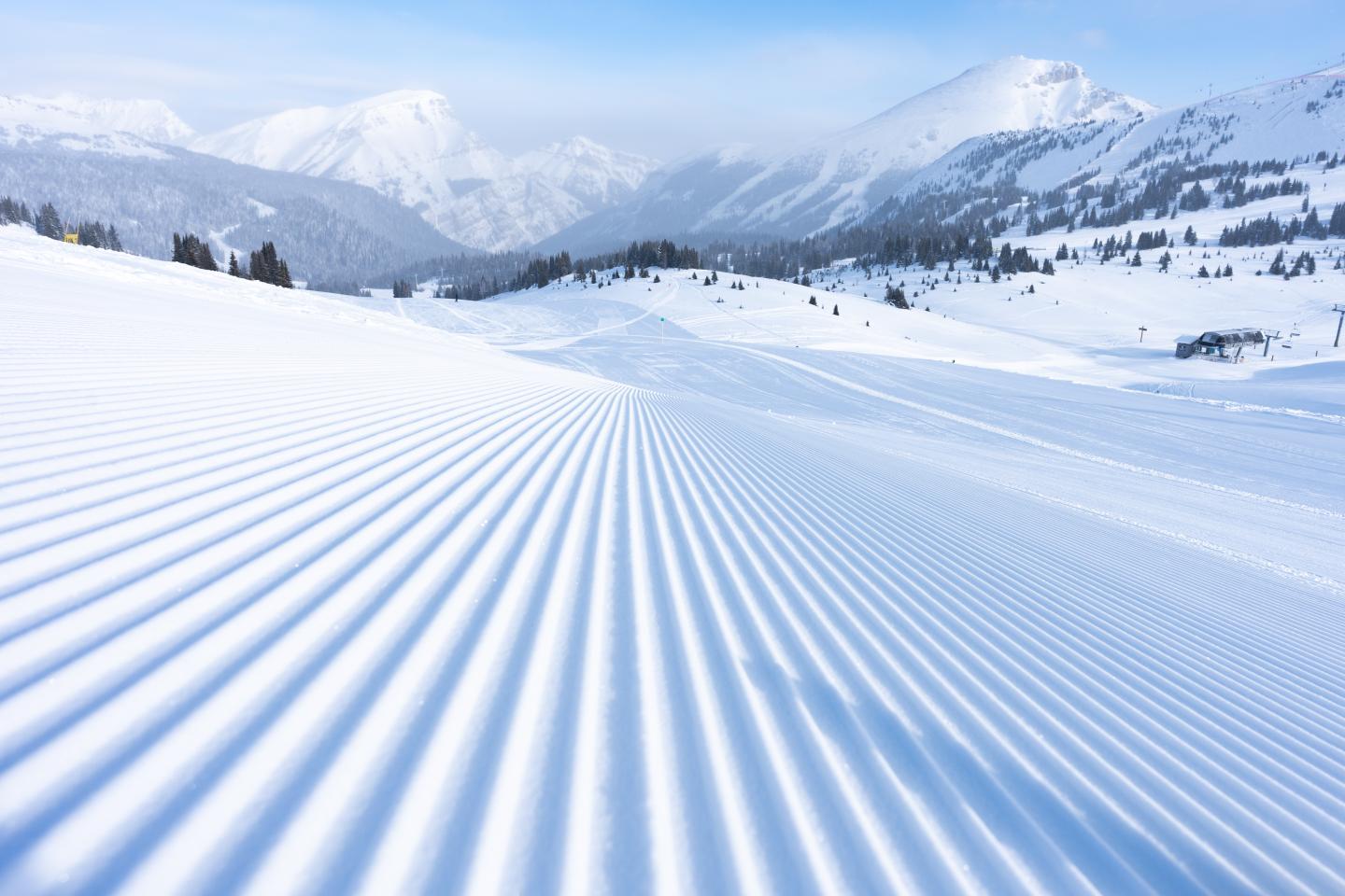 Freshly groomed ski slope with parallel tracks leading toward snowy mountains