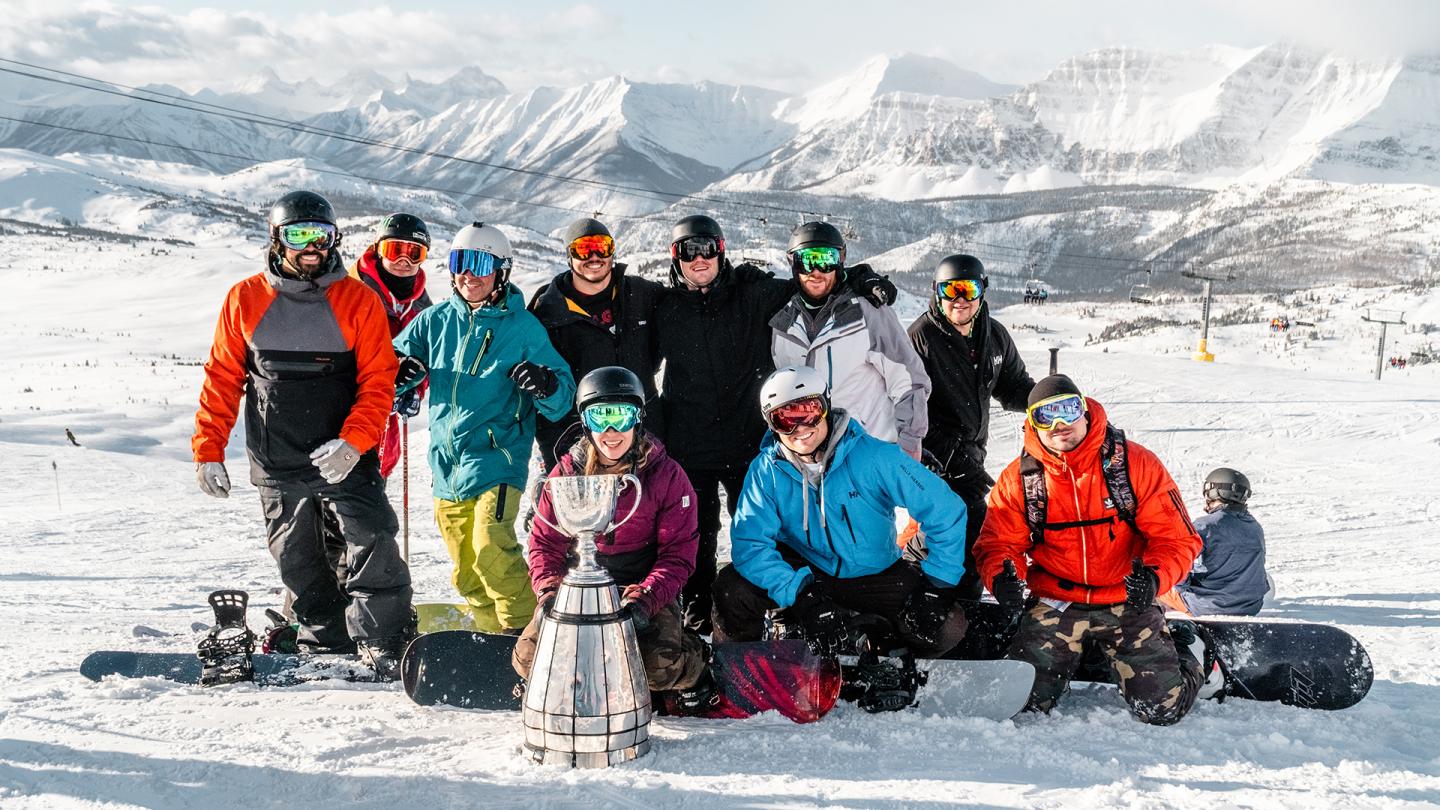 Group of skiers in colorful winter gear posing on a snowy mountain slope.