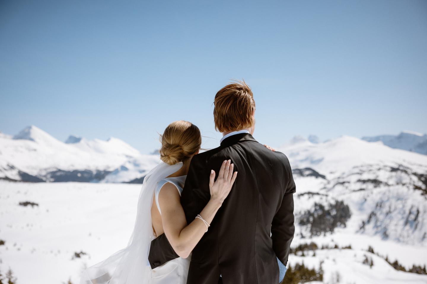 Couple embracing on a snowy mountain overlook under a clear blue sky.