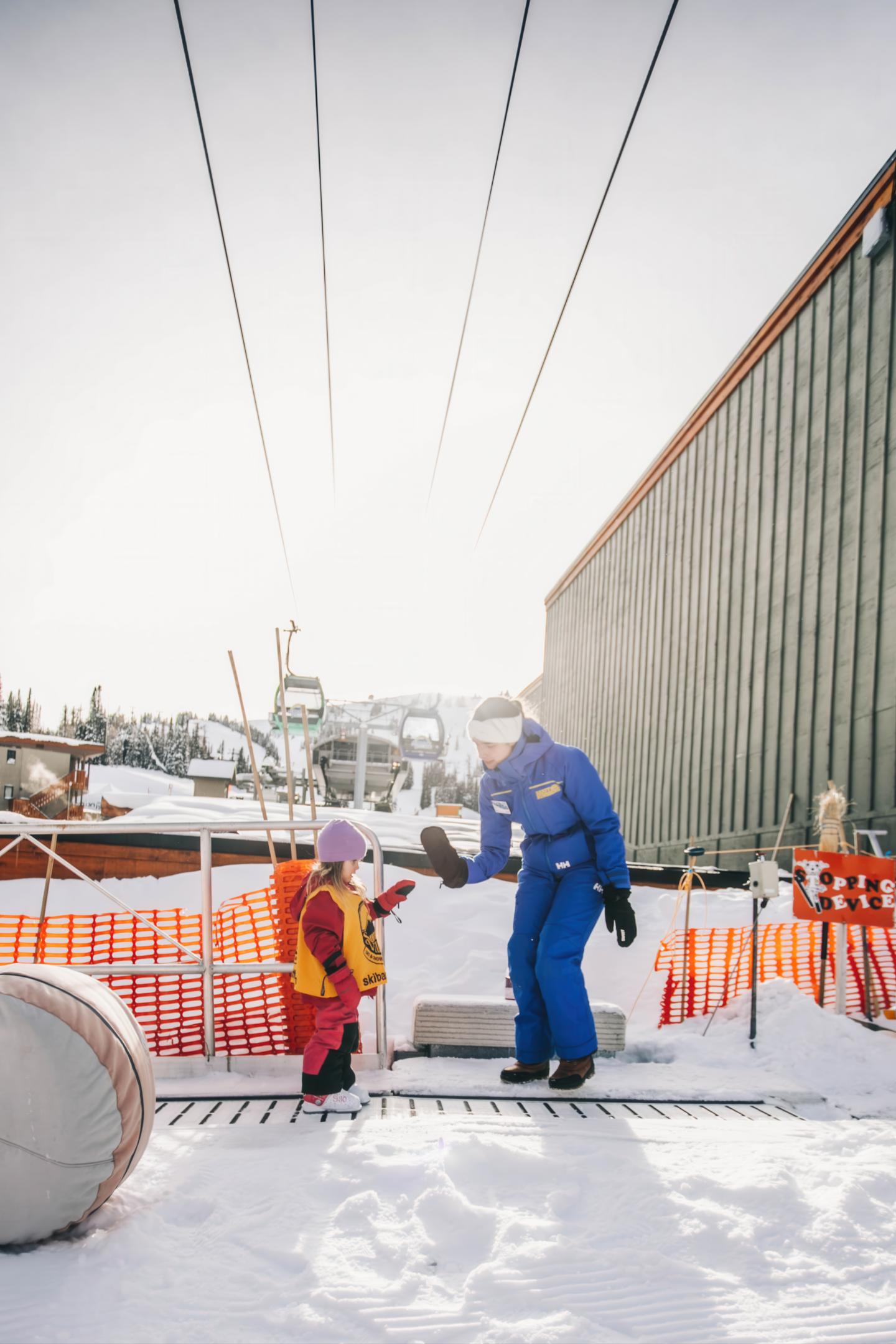Worker in blue winter gear with child beside construction fencing in snow
