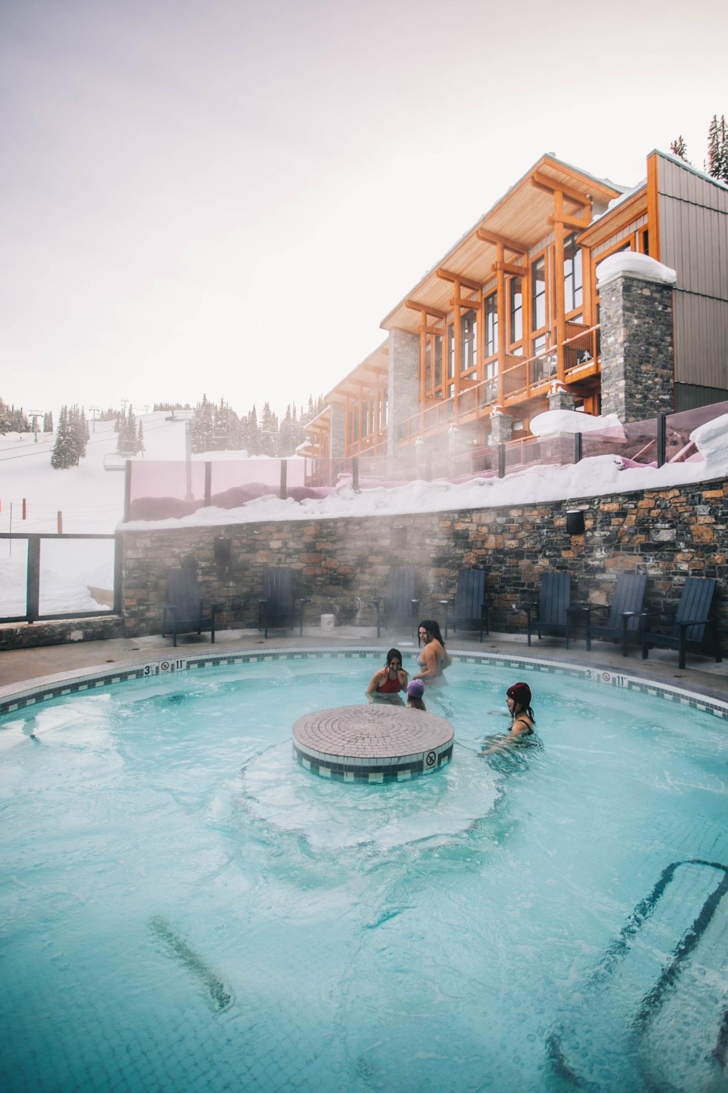 Heated outdoor pool at a snowy mountain lodge, with swimmers and steam rising.