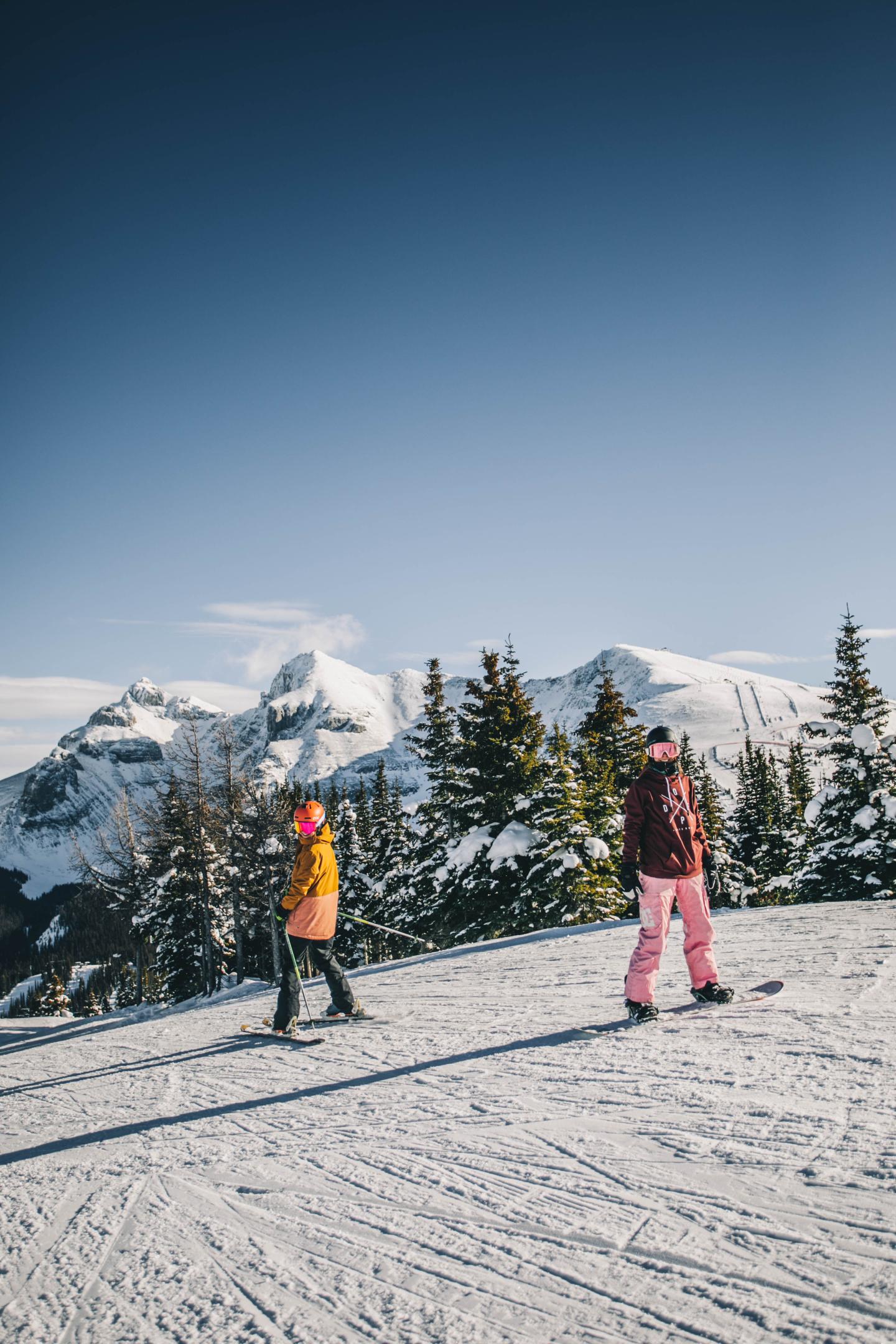 Two skiers in colorful outfits on a snowy mountain slope beneath a clear blue sky.