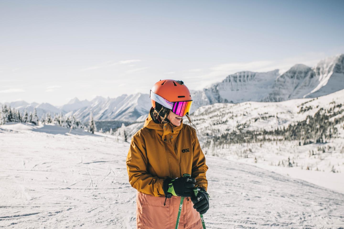 Skier in orange jacket and helmet standing on a snowy mountain slope