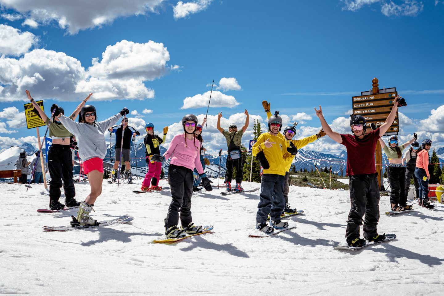 Group practicing yoga poses on a snowy mountain under a bright blue sky.