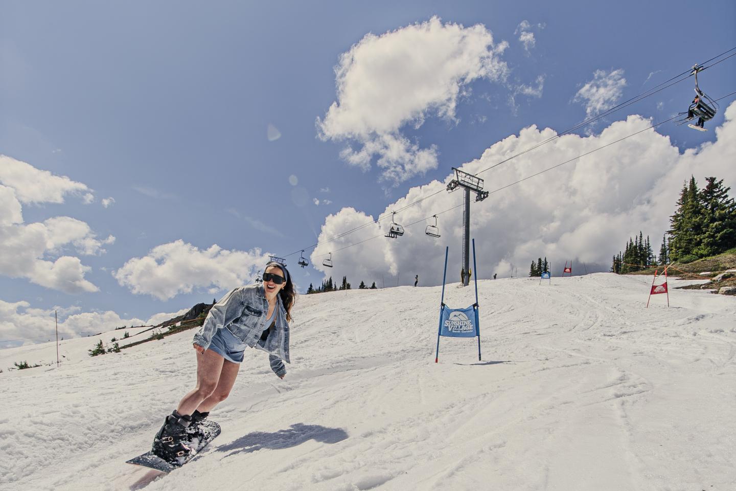 Snowboarder carving down a sunny ski slope beneath chairlifts and clouds