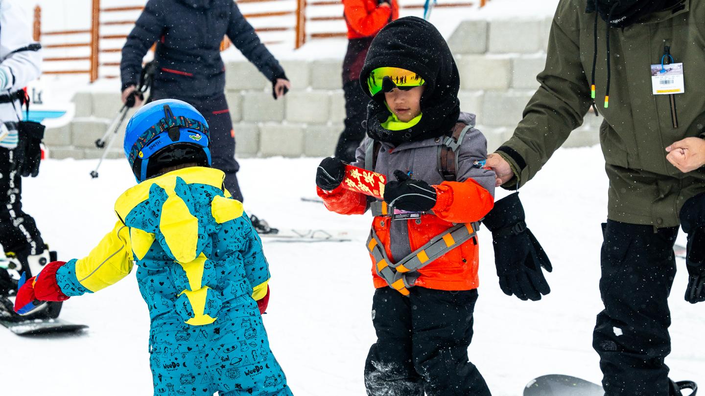 Children in colorful snowsuits skiing with adults on a snowy slope.