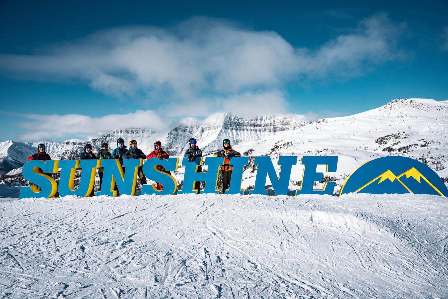 Sunshine logo over snowy mountain slopes beneath a cloudy blue sky