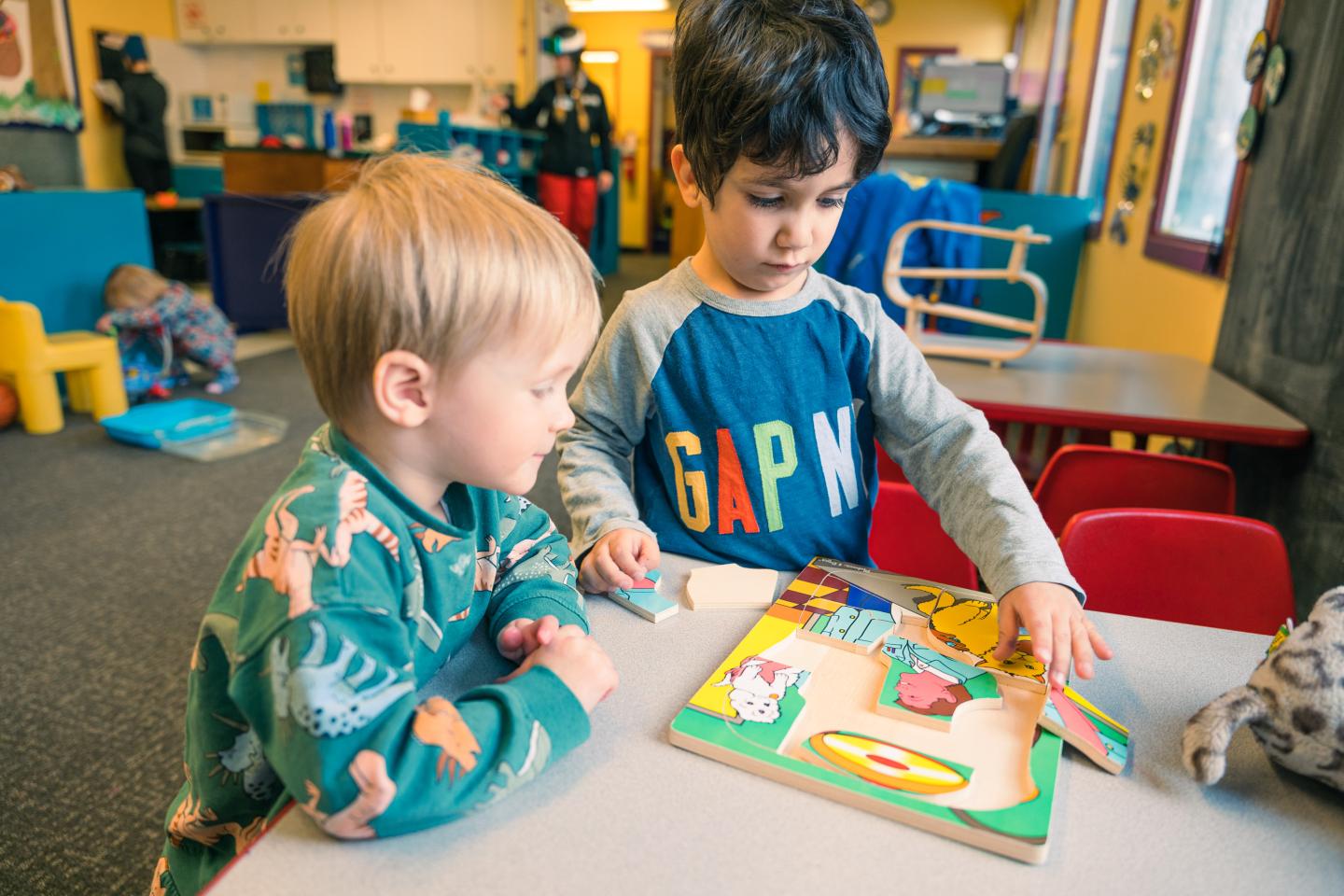 Two young children assembling a colorful puzzle at a classroom table.