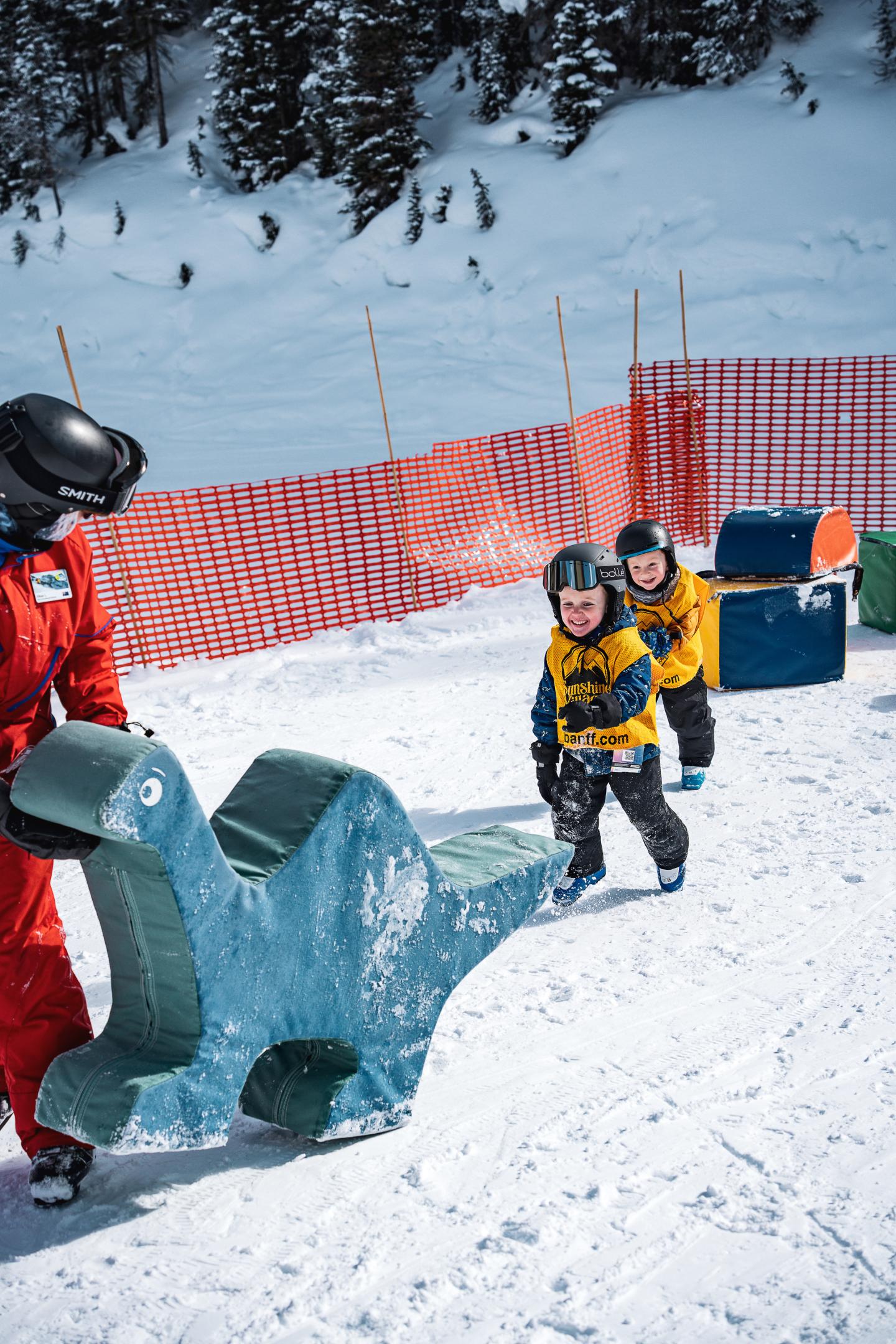 Snowboarder in yellow jacket walking uphill beside skiers on a snowy slope