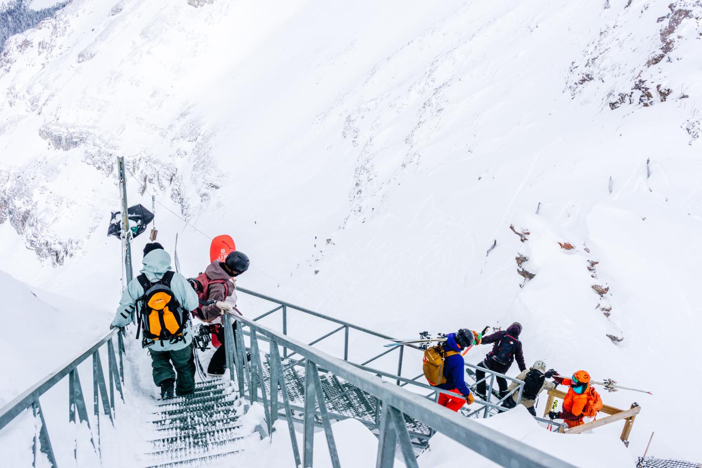 Climbers cross a narrow icy bridge above a snowy mountain slope.