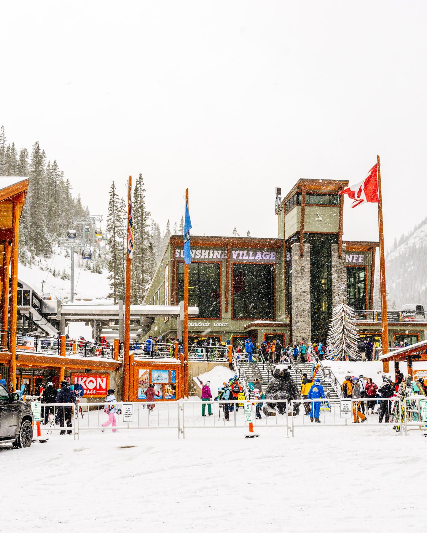 Snowy ski resort plaza with chairlift station, flags, and skiers.